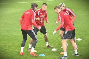 2026 0924 magyar labdarúgó-válogatott edzés fotó-szokodi lászló - szokodi academy media 1 - szokodi academy media Group of soccer players in red training kits circle around on a green field, practicing drills with colored cones nearby.